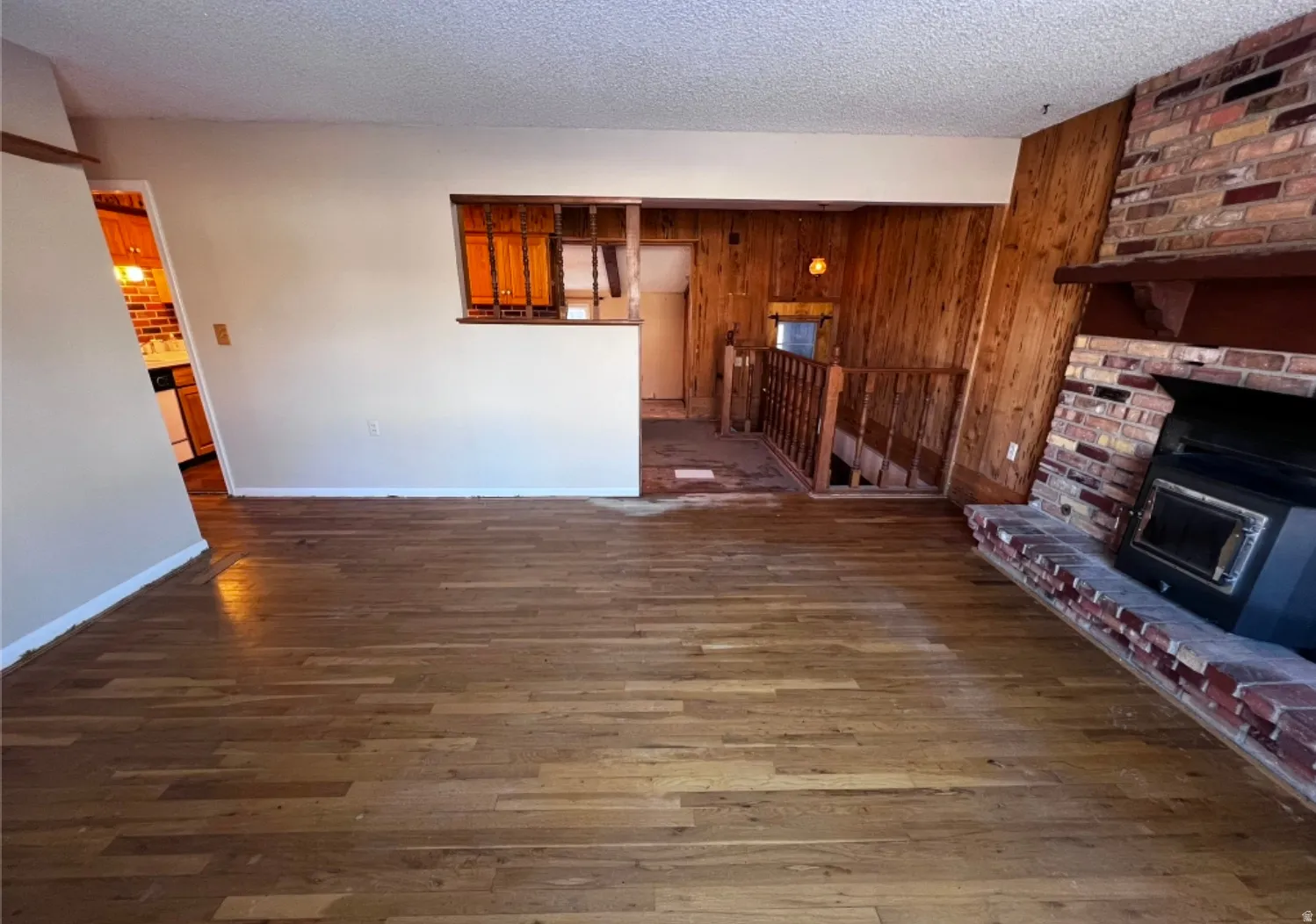 Unfurnished living room featuring wood-type flooring, wooden walls, a fireplace, and a textured ceiling