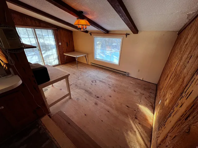 Unfurnished living room with a baseboard radiator, beamed ceiling, and a textured ceiling
