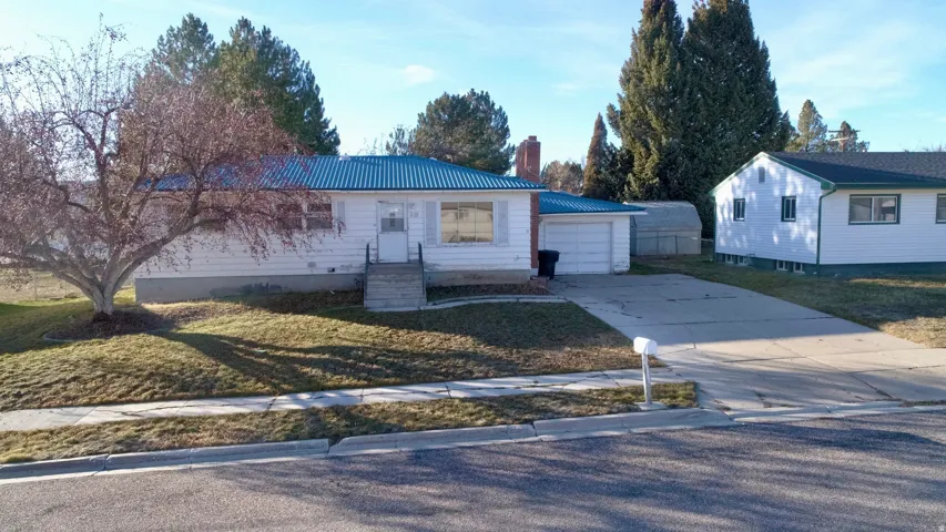 Ranch-style house featuring a metal roof, a front yard, concrete driveway, a chimney, and a garage