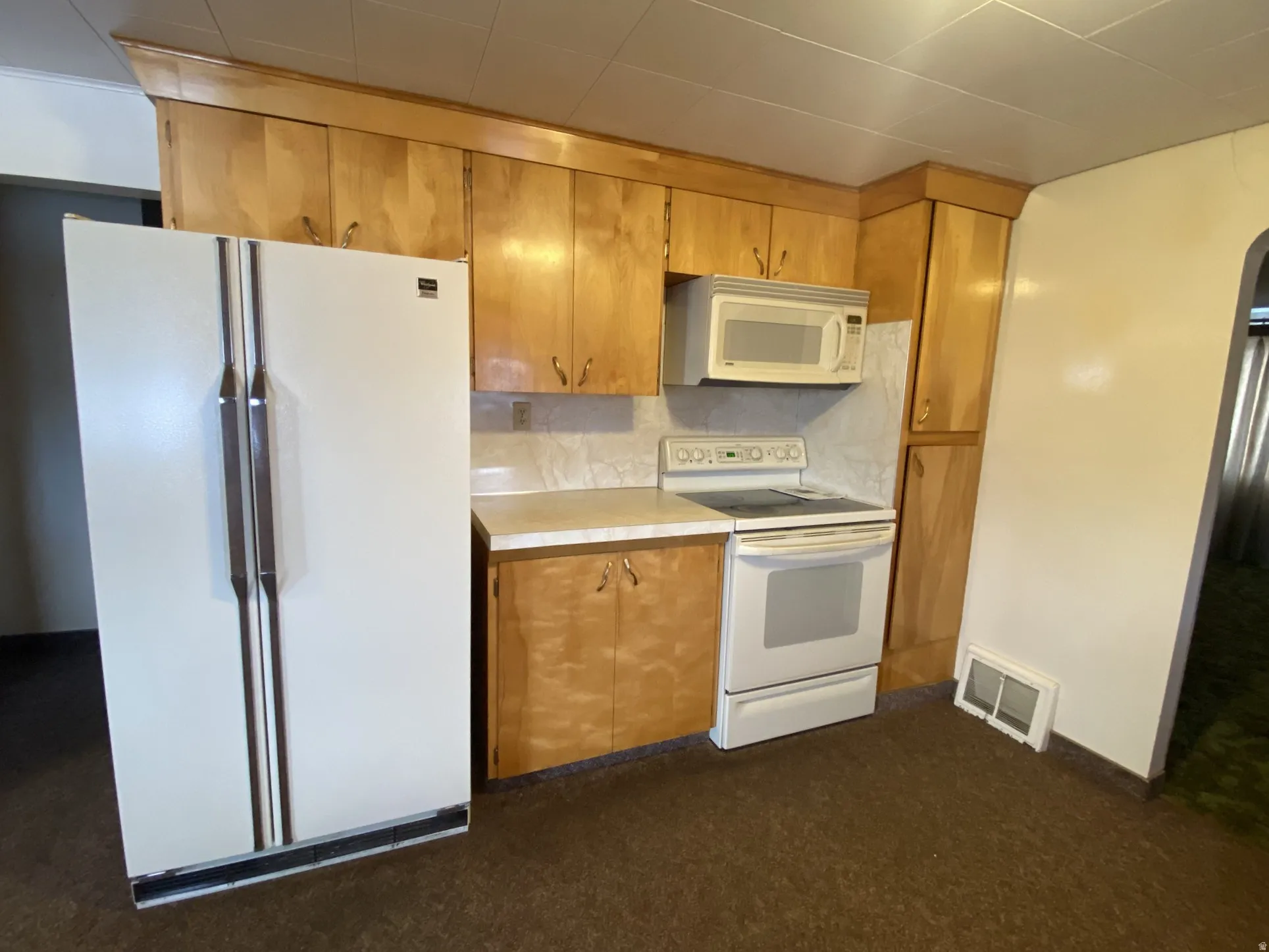 Kitchen featuring white appliances, arched walkways, tasteful backsplash, and brown cabinetry