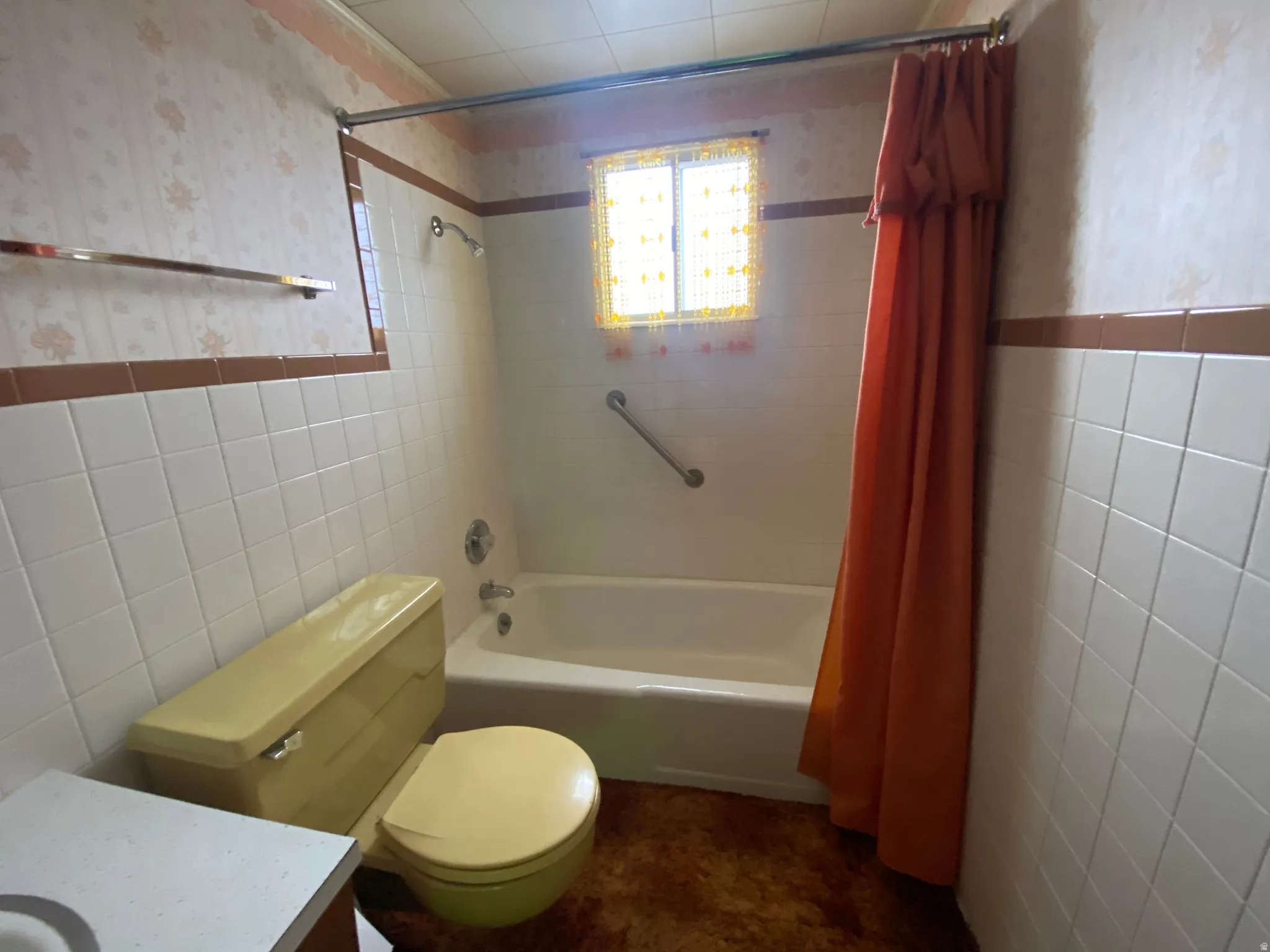 Full bathroom with tile walls, wallpapered walls, shower / bathtub combination with curtain, a wainscoted wall, and vanity