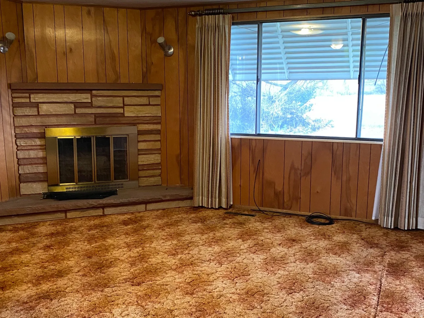 Family room featuring wooden walls, a glass covered wood burning fireplace, and large picture window with a view of the back yard and field.