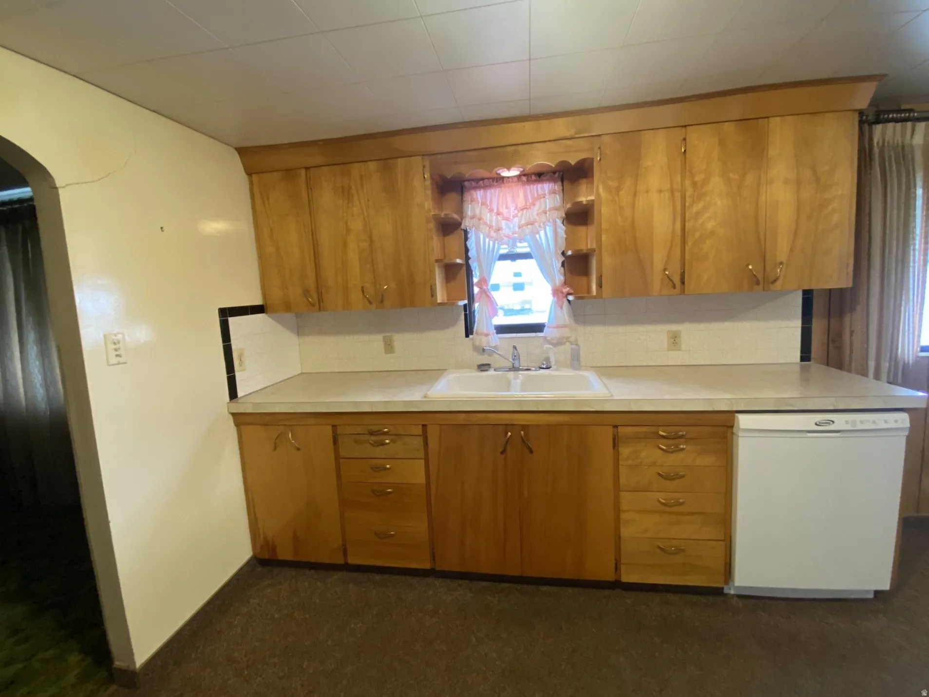 Kitchen with open shelves, tasteful backsplash, brown cabinets, white dishwasher, and arched walkways