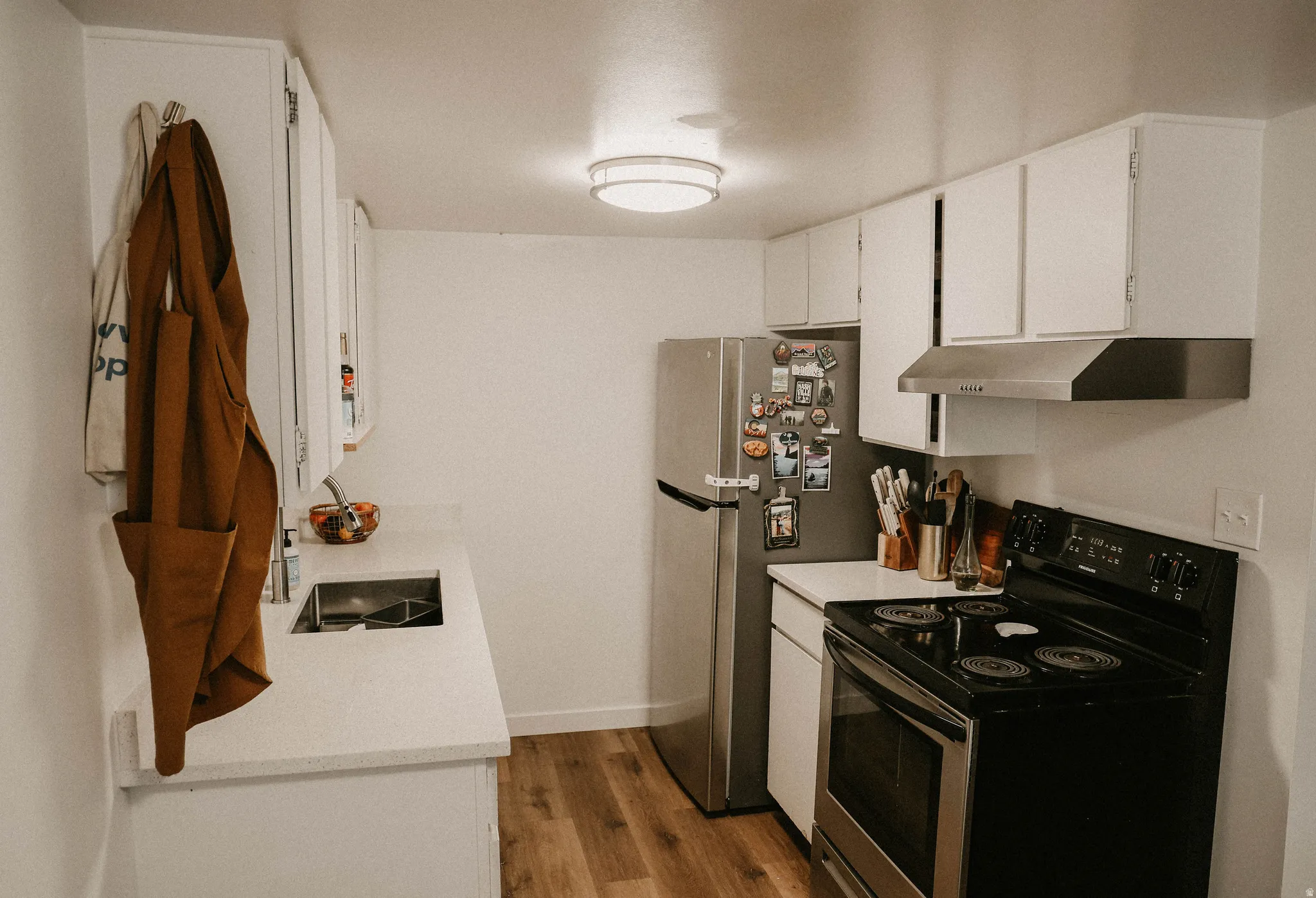 Kitchen featuring black range with electric stovetop, white cabinetry, under cabinet range hood, dark wood-type flooring, and light stone countertops