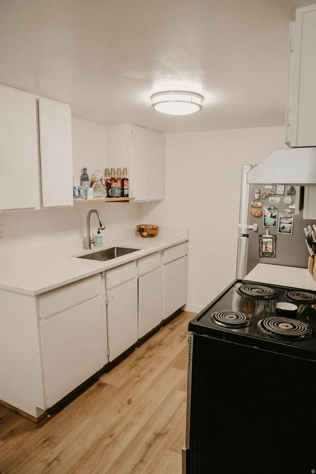 Kitchen featuring black range with electric stovetop, white cabinetry, open shelves, and light countertops