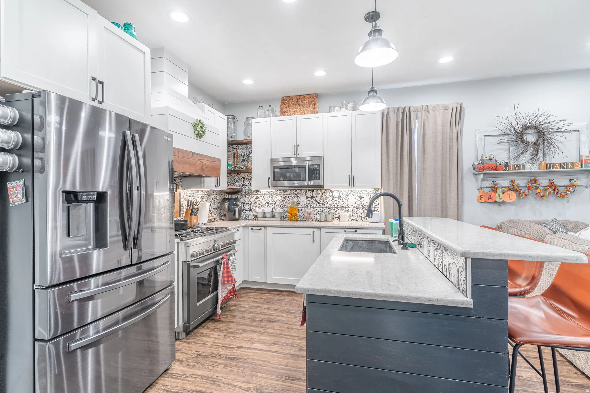 Kitchen featuring stainless steel appliances, white cabinets, a breakfast bar area, hanging light fixtures, and custom exhaust hood
