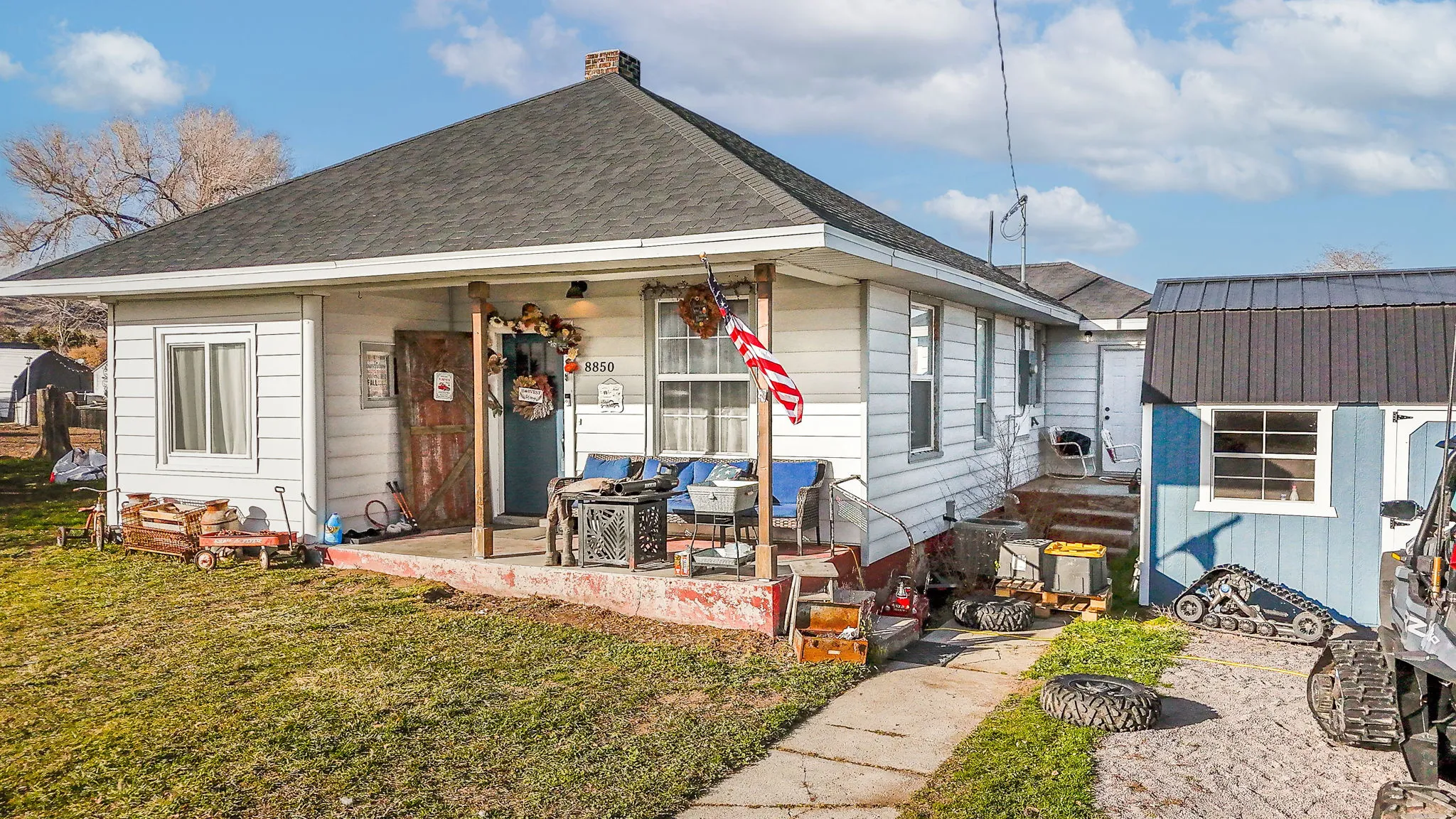 View of front facade with a front lawn, a chimney, roof with shingles, and a storage shed
