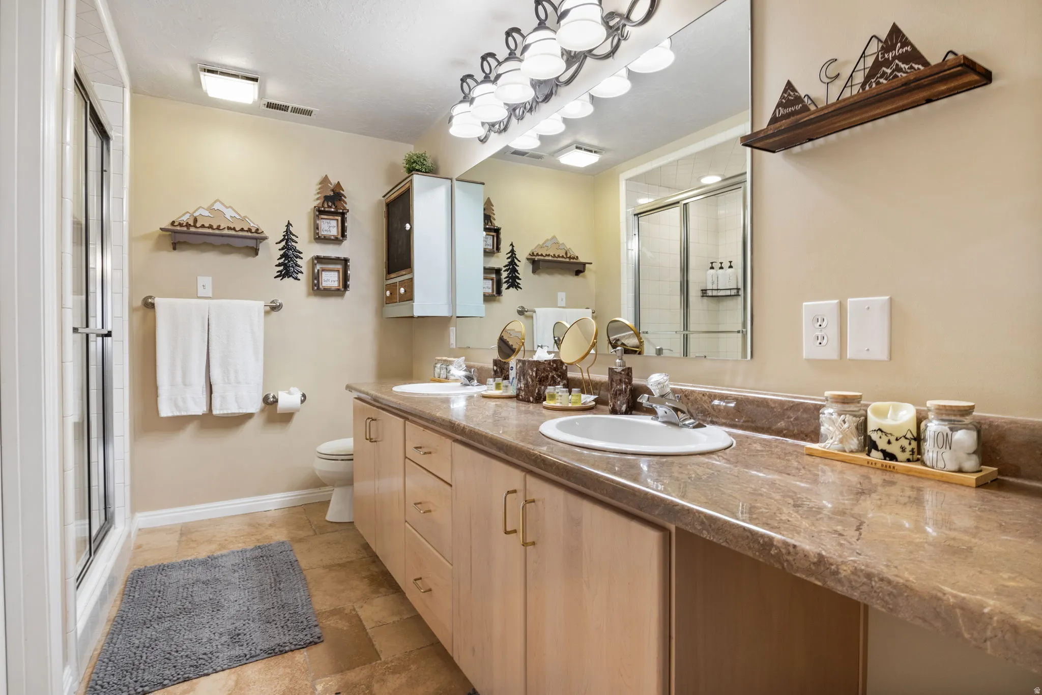 Full bath with double vanity, a stall shower, and stone tile flooring