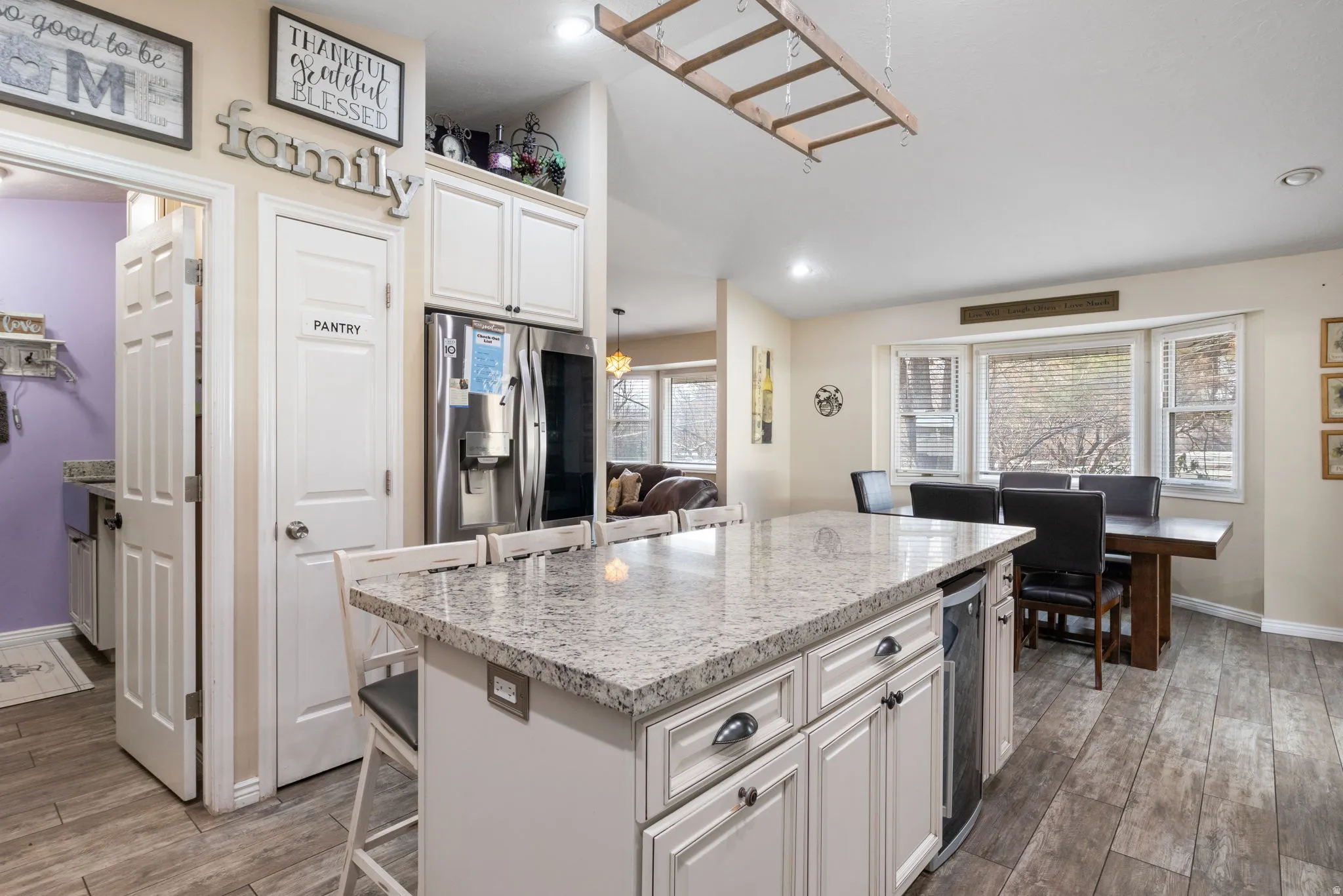 Kitchen with light stone counters, dark wood-style floors, stainless steel fridge, white cabinetry, and recessed lighting