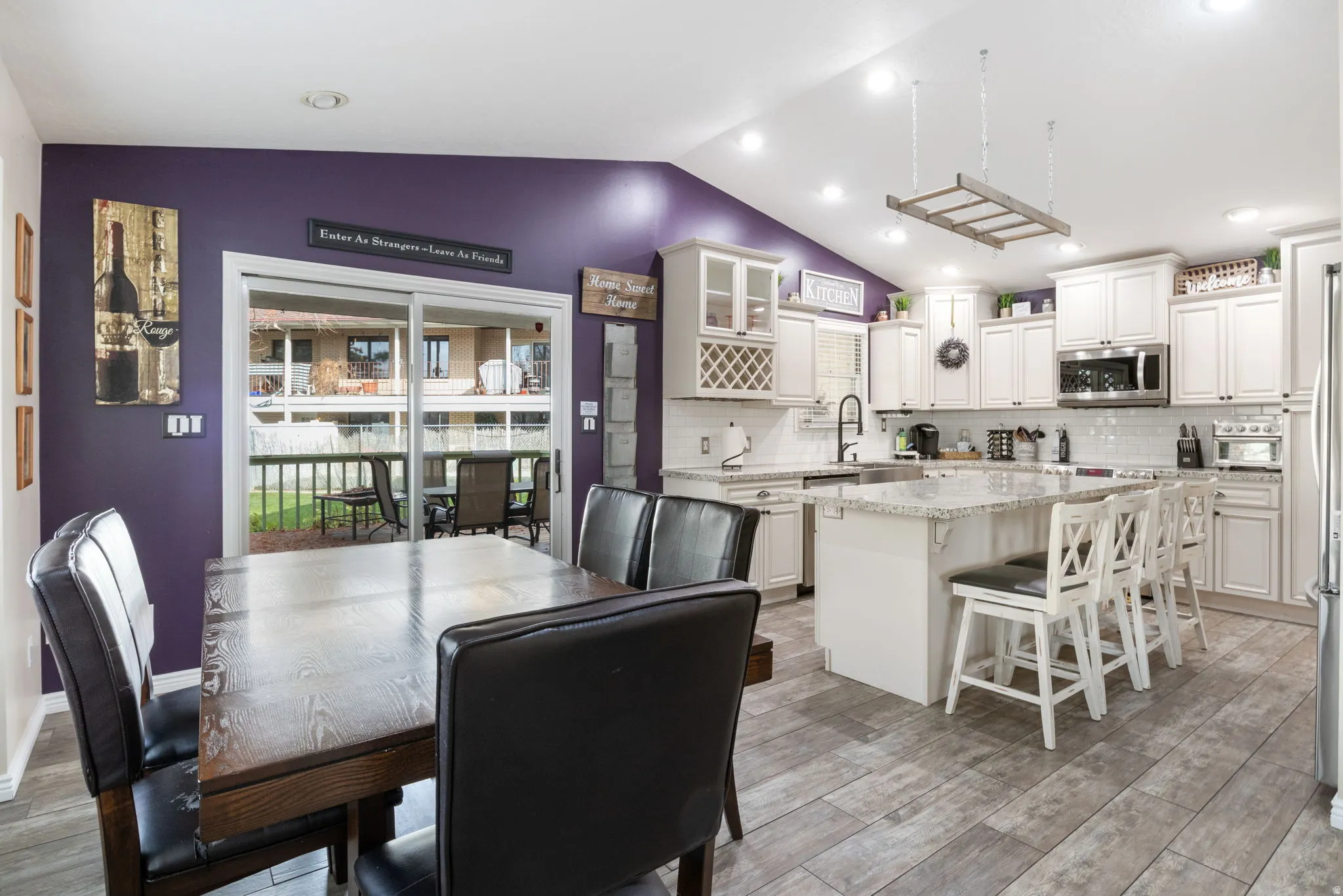 Kitchen featuring vaulted ceiling, a center island, a breakfast bar, white cabinetry, and stainless steel microwave