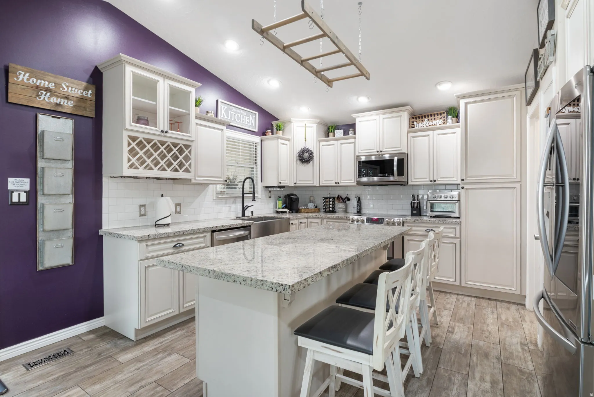 Kitchen featuring lofted ceiling, appliances with stainless steel finishes, backsplash, a kitchen bar, and light stone counters