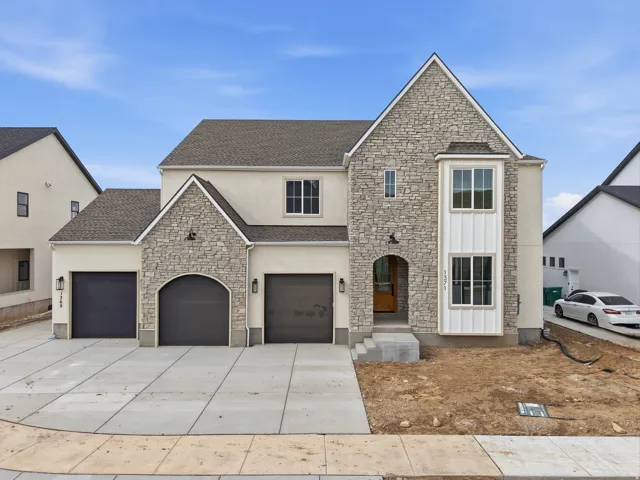 Traditional-style house featuring stone siding, driveway, stucco siding, roof with shingles, and a garage