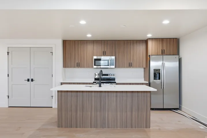 Kitchen featuring wood finish cabinetry, stainless steel appliances, recessed lighting, a kitchen island with sink, and light wood-style floors