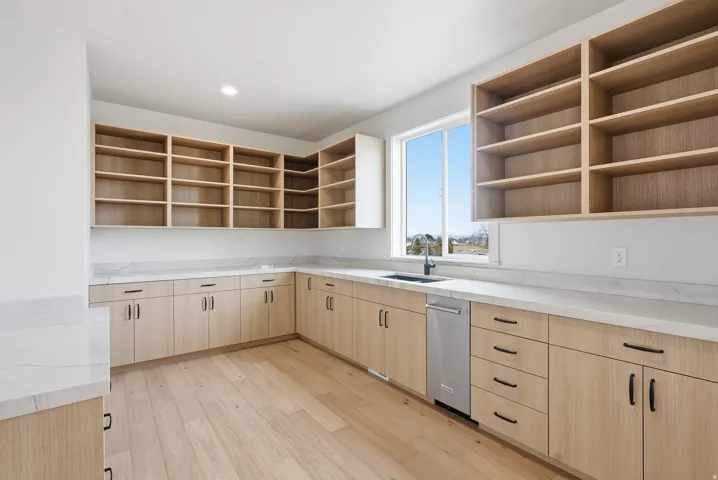 Kitchen featuring light wood finish cabinetry, open shelves, light stone countertops, light wood-style floors, and dishwasher