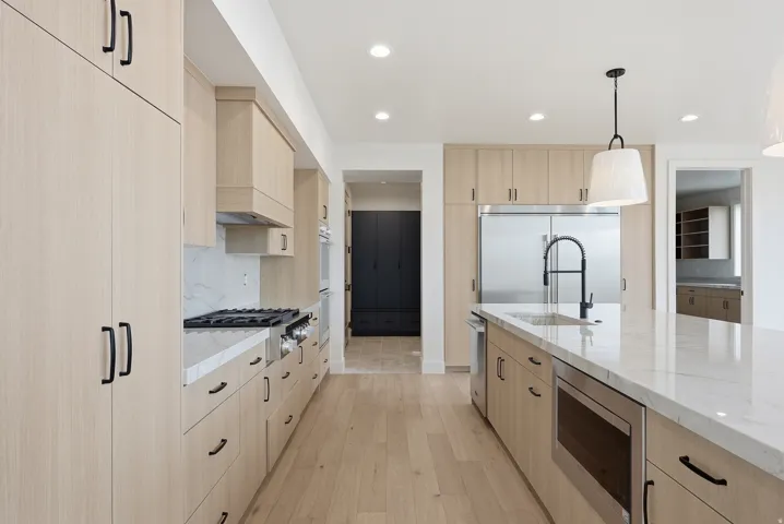 Two tone kitchen with decorative light fixtures, light stone countertops, light wood-style floors, built in appliances, and modern cabinets
