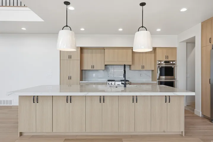 Kitchen featuring light wood finish cabinets, light stone counters, light wood-style flooring, and a spacious island