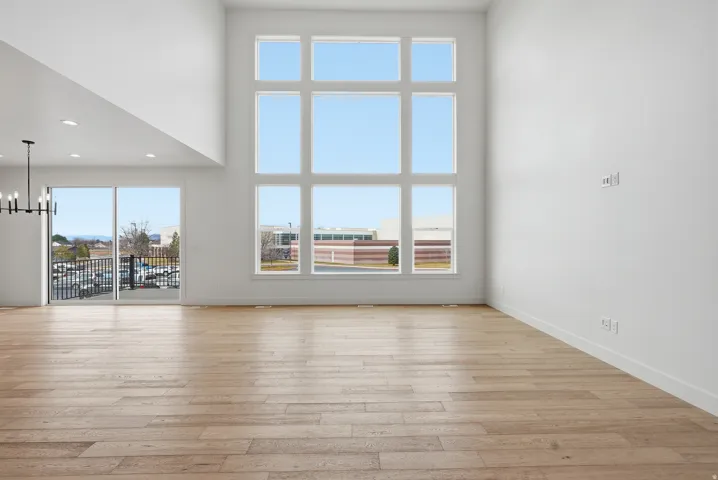 Unfurnished living room featuring a high ceiling, healthy amount of natural light, a chandelier, and light wood finished floors