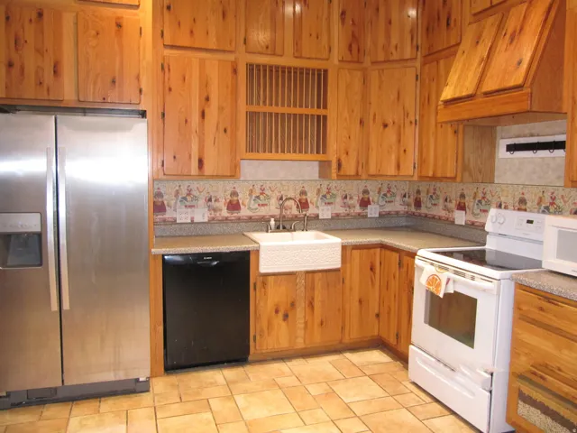 Kitchen featuring white appliances, custom range hood, light countertops, and brown cabinets