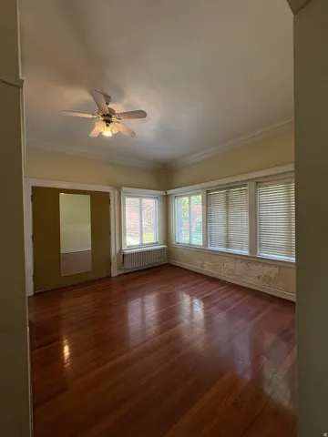 Room featuring wood-finish flooring, a ceiling fan, and multiple windows with blinds