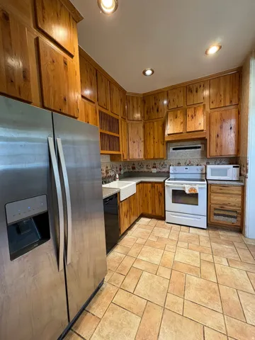 Kitchen featuring extensive wood cabinetry, stainless steel refrigerator, white farmhouse sink, white electric range, and tile flooring