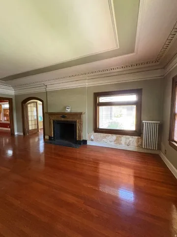 Hardwood flooring throughout, featuring a decorative fireplace with a substantial mantel, ornate crown molding, a coffered ceiling, and glass-paneled double doors
