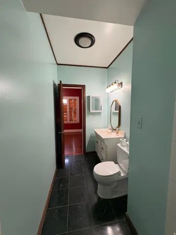 Bathroom featuring a single vanity with a white countertop and base cabinetry, a wall-mounted mirror, and a toilet