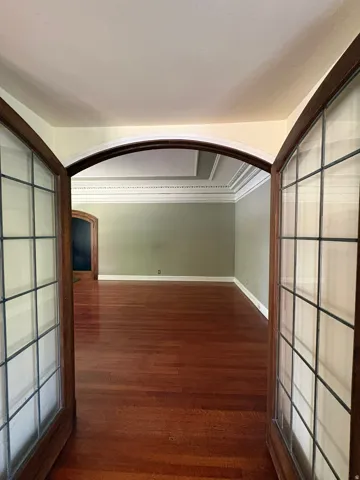 Double doors with leaded glass panels open to an interior space featuring wood-finish flooring, an arched entryway, detailed crown molding, and a tray ceiling