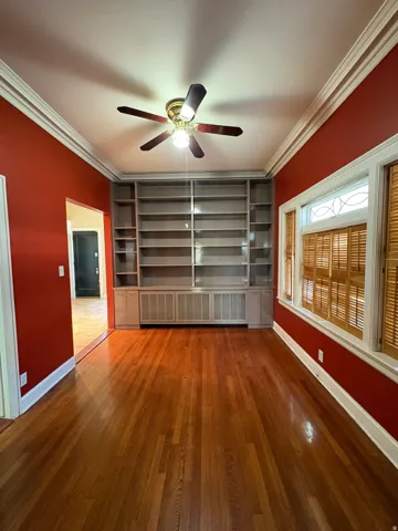 Interior room featuring built-in shelving, hardwood flooring, a ceiling fan, and plantation shutters