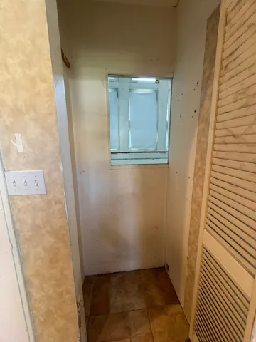 Small interior alcove featuring a square window opening, tile flooring, and a louvered bifold door