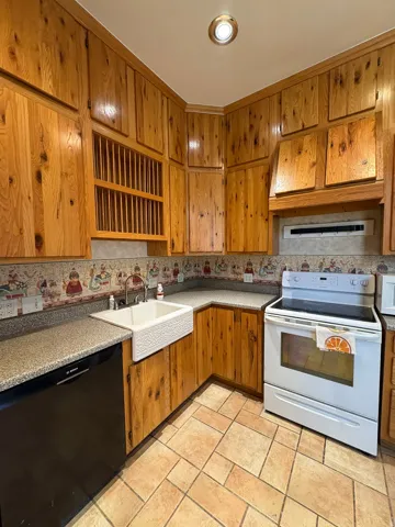 Kitchen featuring extensive wood cabinetry, a farmhouse-style sink, solid surface countertops, and tile flooring
