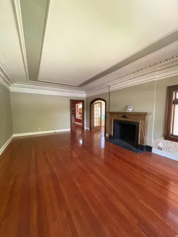Spacious interior featuring wood-finish flooring, an ornate decorative fireplace with a dark stone hearth, detailed crown molding, a coffered ceiling, and a prominent arched entryway