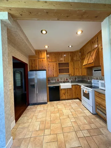 Kitchen featuring extensive wood cabinetry, stainless steel refrigerator, black dishwasher, and a white farm sink