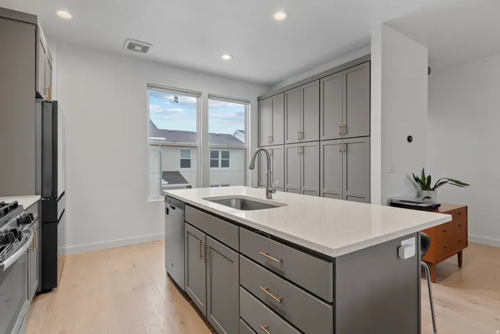 Kitchen featuring gray cabinetry, light stone counters, an island with sink, stainless steel appliances, and light wood-style floors