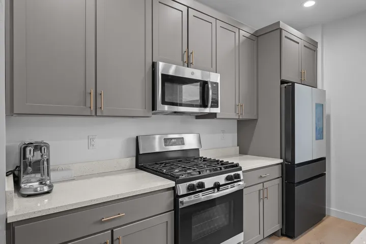 Kitchen featuring gray cabinetry, stainless steel appliances, light stone counters, light wood-style floors, and recessed lighting
