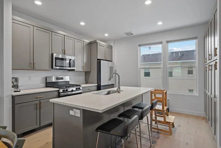Kitchen with gray cabinets, stainless steel appliances, light wood-style floors, a center island with sink, and recessed lighting
