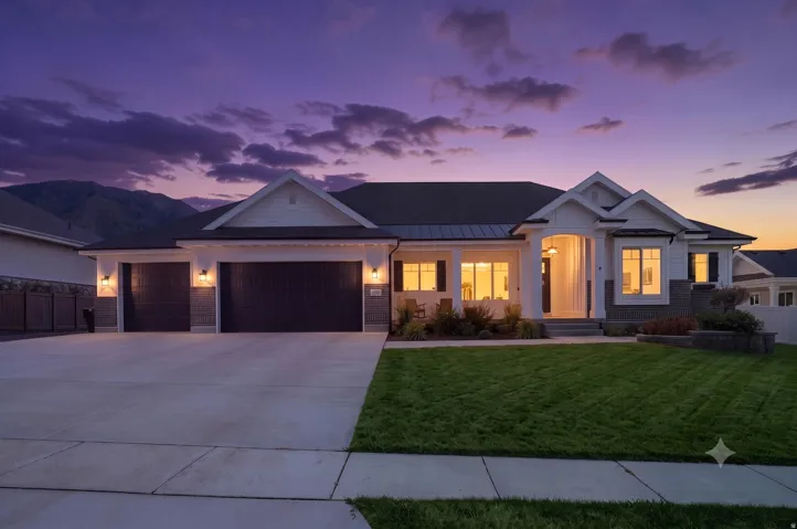 Modern farmhouse-style exterior featuring a covered front porch, dual two-car garages, a manicured lawn, and mountain scenery