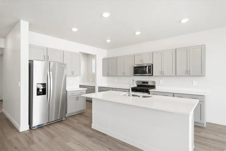 ***DISCLAIMER** Exterior & Interior finishes may vary. Kitchen featuring appliances with stainless steel finishes, gray cabinets, light wood-style flooring, an island with sink, and light stone counters