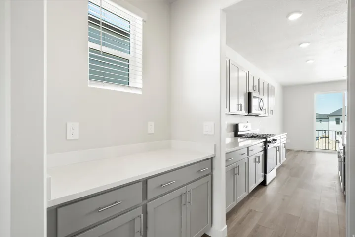 ***DISCLAIMER** Exterior & Interior finishes may vary. Kitchen with gray cabinets, appliances with stainless steel finishes, light wood-style floors, recessed lighting, and light stone countertops