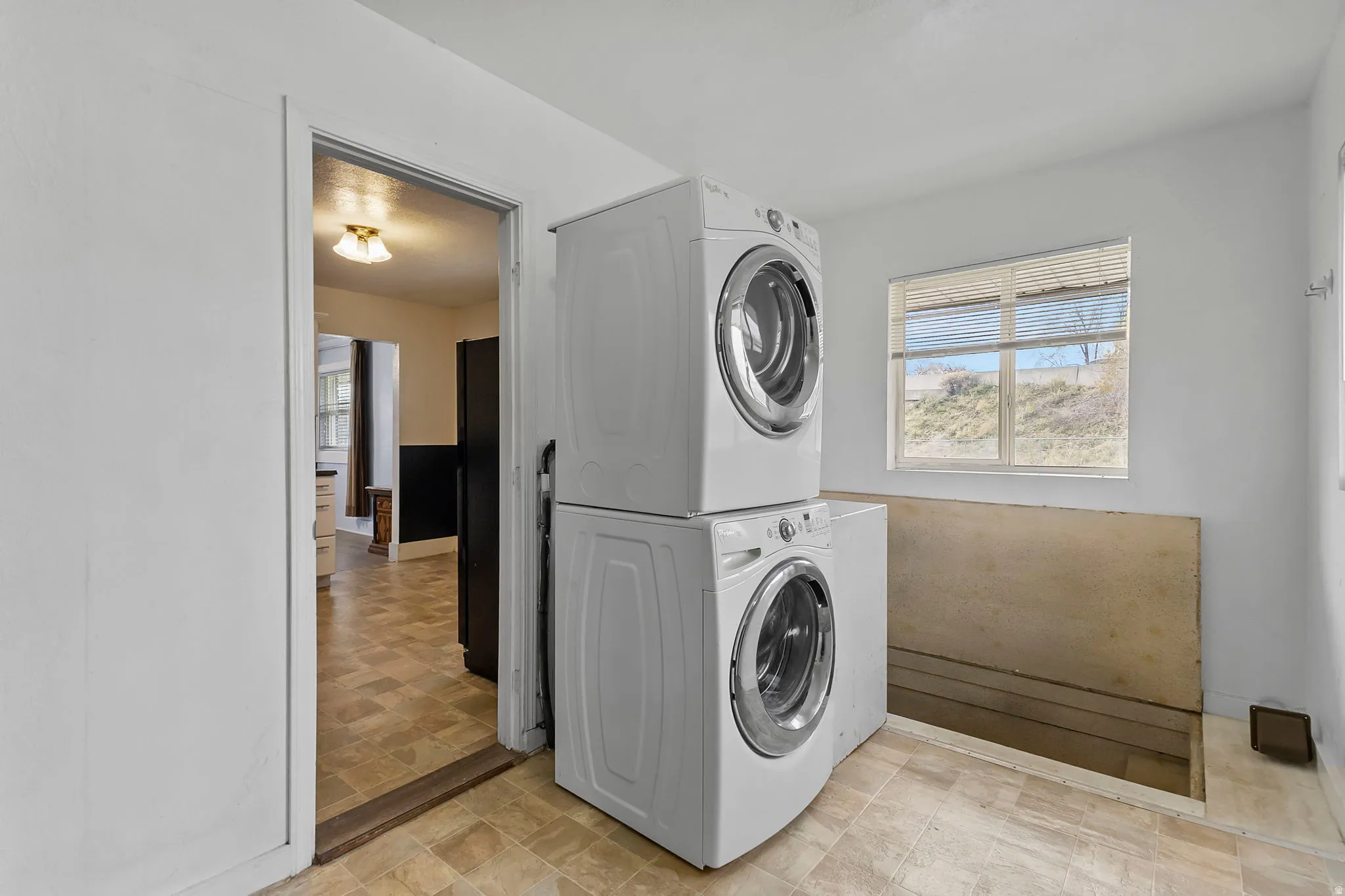 Laundry area with stacked washing machine and dryer and stone finish flooring