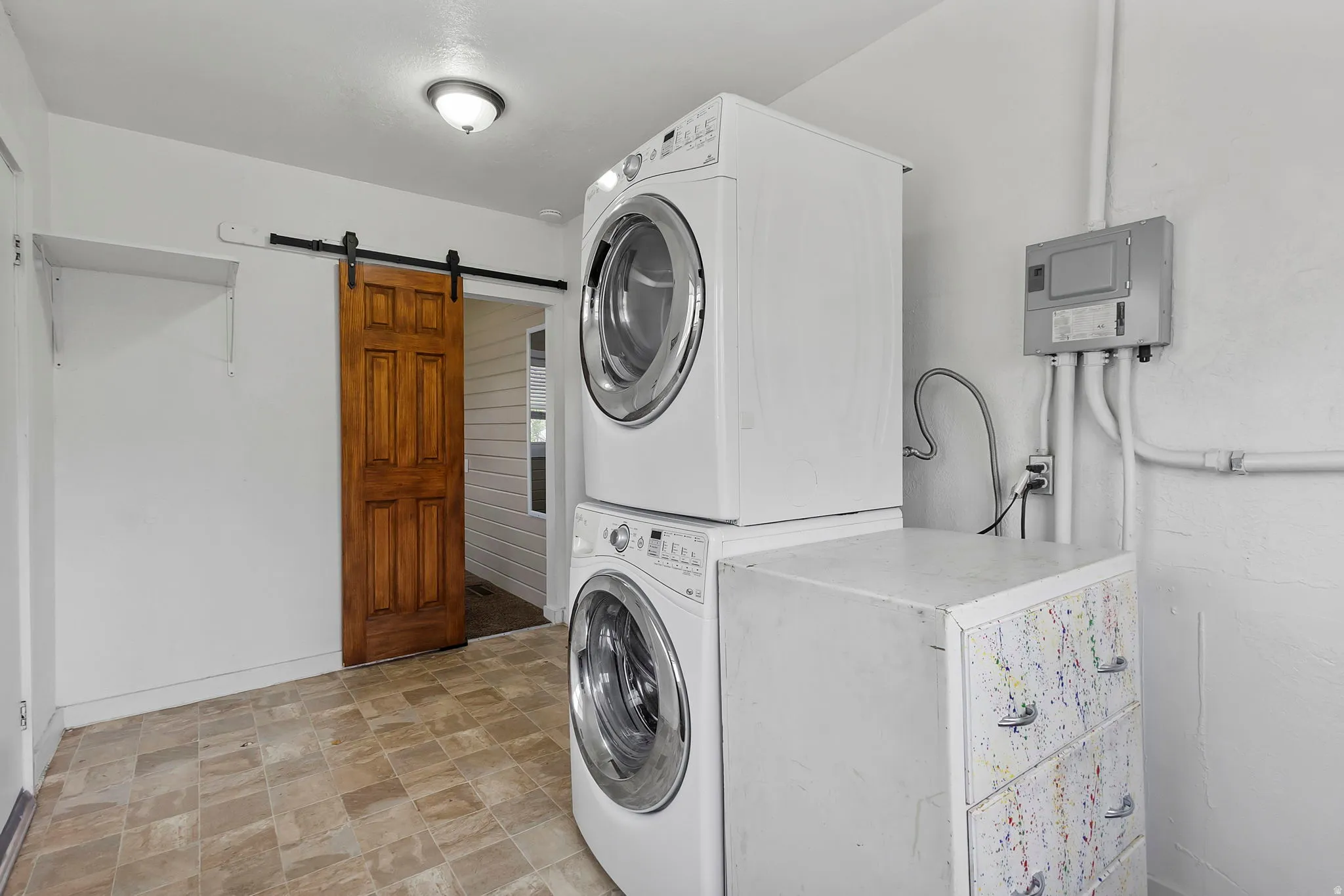 Laundry room with stone finish floors, stacked washer / dryer, and a barn door
