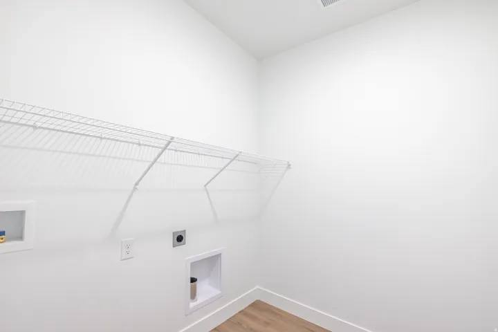 Dedicated laundry area with white wire shelving, utility hookups, and wood-finish flooring