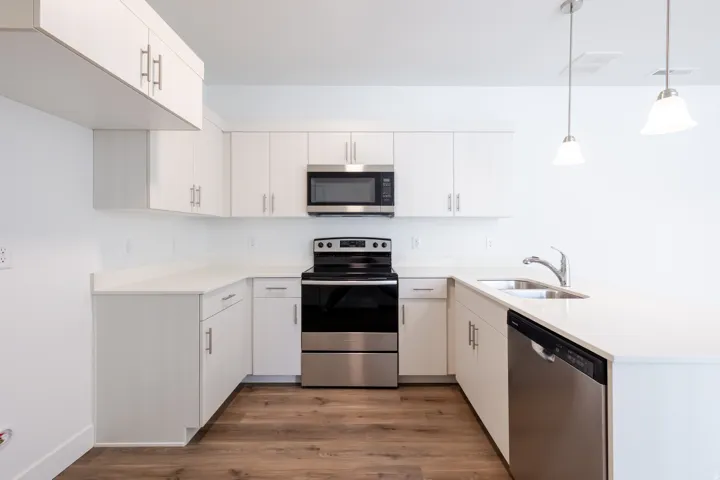 Bright kitchen featuring white cabinetry, light countertops, wood-finish flooring, stainless steel appliances, and pendant lighting