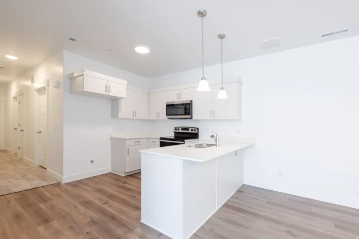Modern kitchen featuring white cabinetry, light-toned countertops, stainless steel appliances, and wood-finish flooring