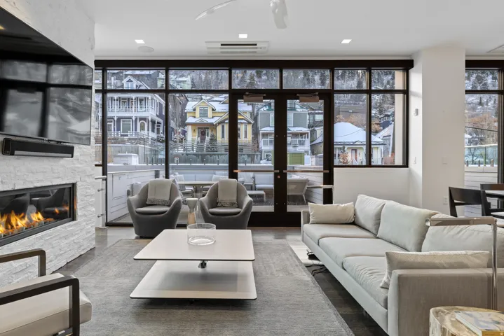 Living room with floor to ceiling windows, a stone fireplace, and wood finished floors