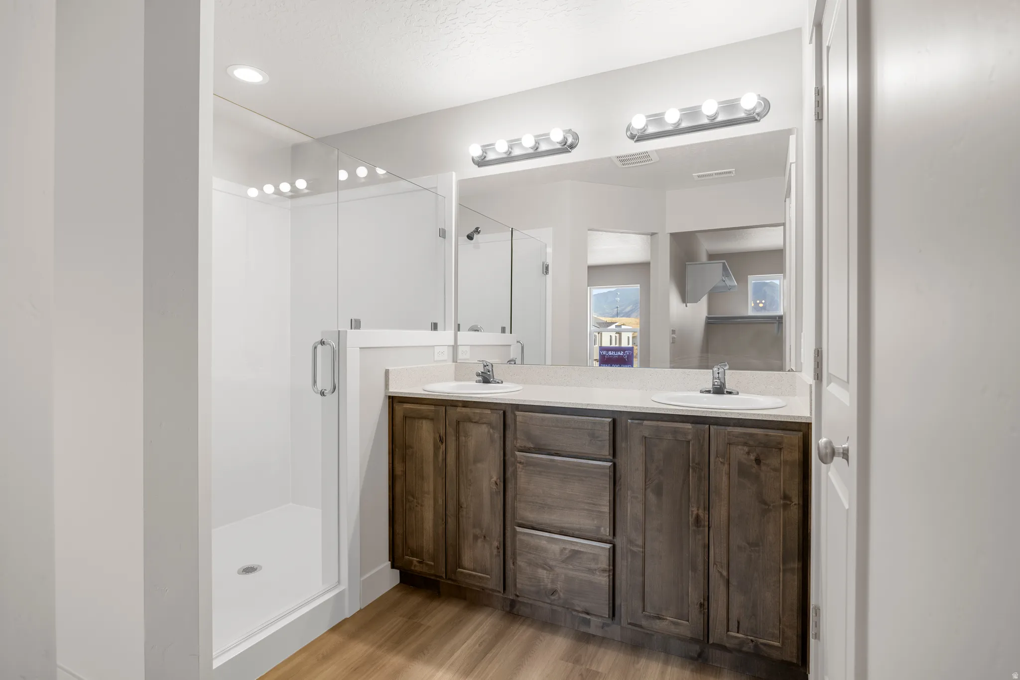 Bathroom featuring double vanity, light wood-style flooring, a shower stall, and a textured ceiling