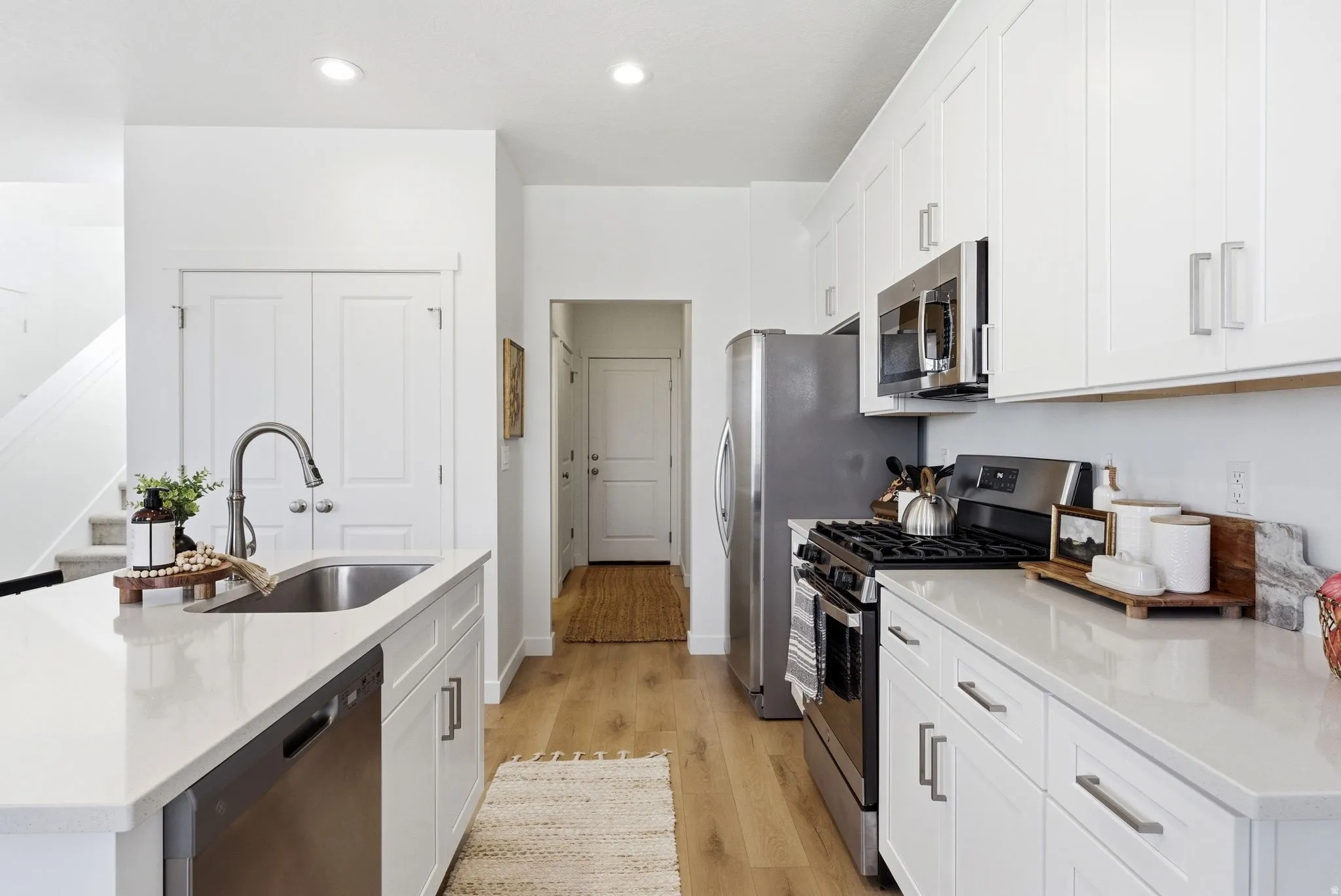 Kitchen featuring stainless steel appliances, light stone counters, light wood-type flooring, white cabinetry, and a kitchen island with sink