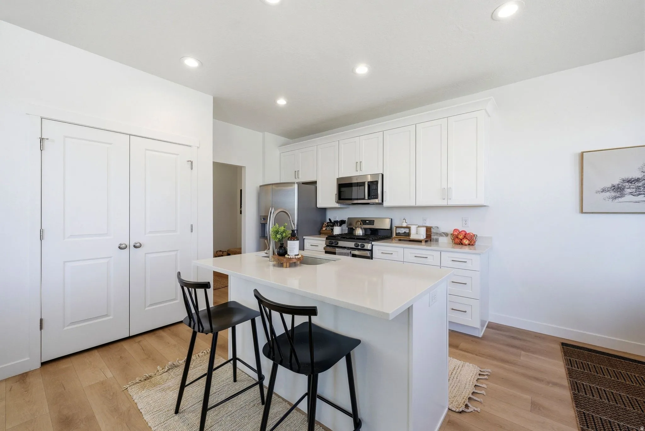 Kitchen with an island with sink, white cabinetry, stainless steel appliances, light wood-style floors, and recessed lighting