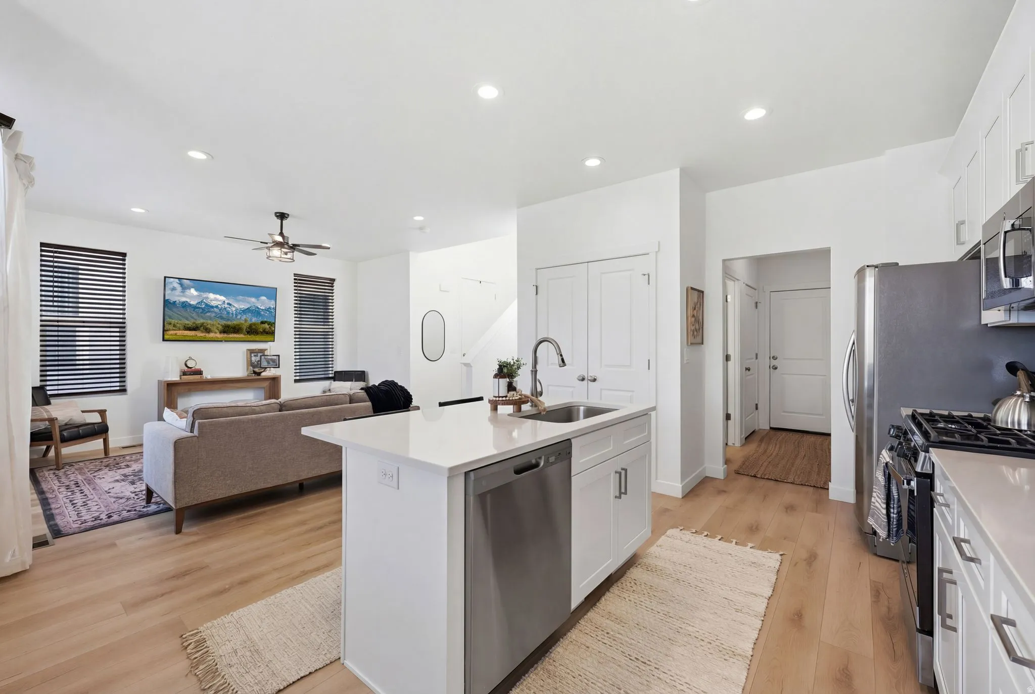 Kitchen with an island with sink, stainless steel appliances, light wood finished floors, open floor plan, and white cabinets