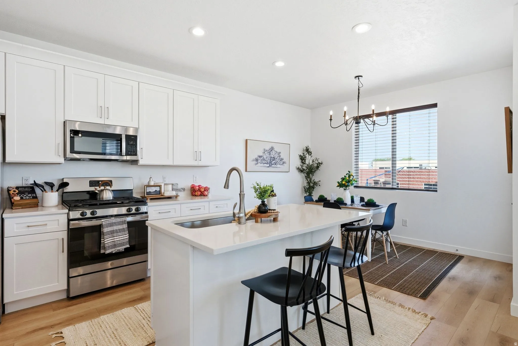 Kitchen with stainless steel appliances, a kitchen island with sink, white cabinetry, and light wood finished floors