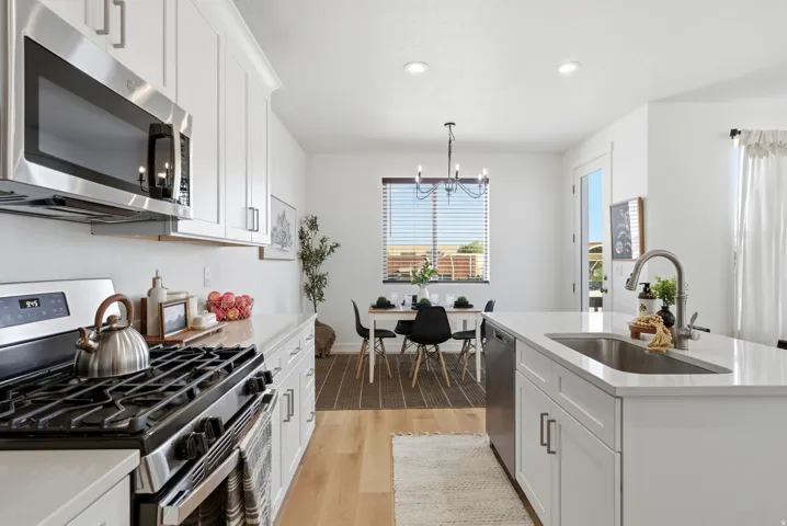 Kitchen featuring stainless steel appliances, white cabinetry, light wood-style flooring, light stone counters, and a kitchen island with sink